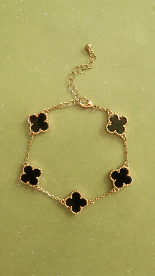 Gold bracelet with black clover-shaped charms on a green background